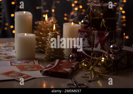 le candele e i regali avvolti con luce fotografica si trovano sul tavolo con un ghirland sullo sfondo Foto Stock