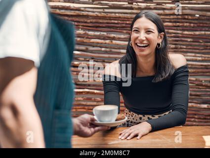 Felice giovane donna ispanica che riceve una tazza di caffè da un cameriere in un bar locale. Donna di razza mista entusiasta di essere servita il suo latte caldo o cappuccino Foto Stock