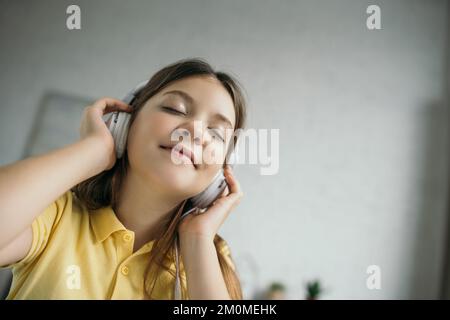 vista dal basso angolo di una ragazza premiuta con occhi chiusi che ascolta la musica con le cuffie Foto Stock