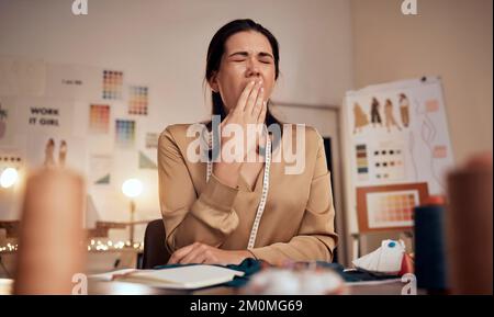 Stilista di moda stanco, donna e sbadiglio mentre lavora di notte in ufficio creativo, studio tessile o startup. Sarto esausto, assonnato e sovraccarico di lavoro Foto Stock
