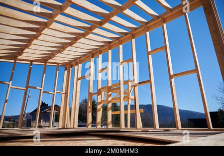 Vista dal basso della casa con telaio in legno su fondamenta in pile in costruzione su sfondo cielo blu. Foto Stock