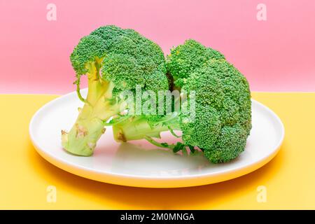 Due pezzi freschi e grezzi di broccoli su piastra bianca. Cavolo verde non fatto. Cultura vegana e vegetariana. Cibo crudo. Alimentazione sana e dieta vegetale Foto Stock