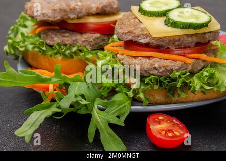 Cheeseburgers con cetriolo, verdure, cipolle tritate e carote su piatto grigio. Primo piano. Sfondo nero. Foto Stock