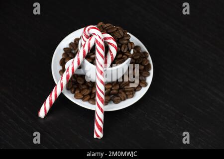 Caramelle natalizie e chicchi di caffè in tazza bianca su tavola di legno scuro. Caffè arrosto scuro, bevanda naturale per le vacanze invernali Foto Stock