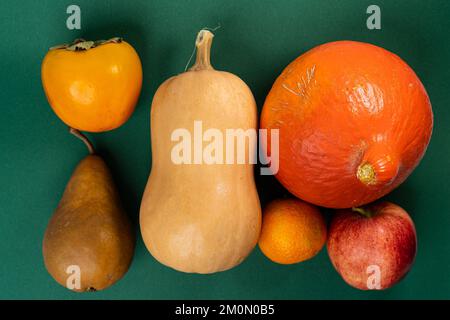 Zucca, mela, pera, mandarino e persimmone su sfondo verde Foto Stock