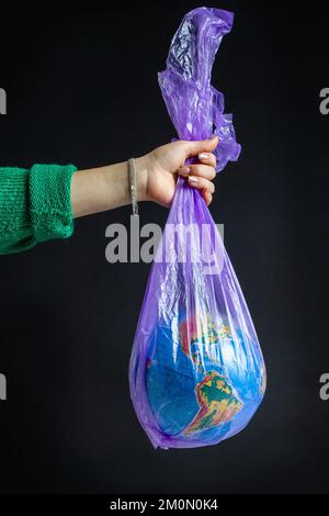 Borsa di plastica per mano femmina con globo mondiale. Isolato su sfondo nero. Foto Stock