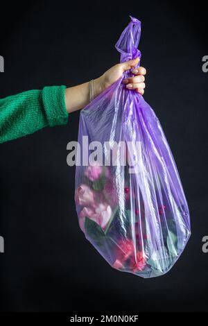 Chiudere la mano delle donne che tiene il sacchetto di plastica con i fiori. Isolato su nero. Concetto di spreco di denaro. Foto Stock