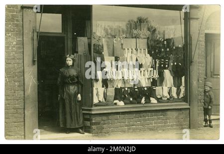 Originale affascinante post edoardiano / Titanic era cartolina del proprietario signora o assistente di vendita in piedi fuori di un negozio di abbigliamento maschile, nella finestra di cui pubblicizza le vendite di cravatte, camicie, lane, calze. C'è un bambino di un vicino che sbirciava da una porta dietro l'angolo. Un classico "moment in time" catturato. La cartolina è datata / pubblicata il 31 maggio 1911 da Warrington, Cheshire, Inghilterra, Regno Unito Foto Stock