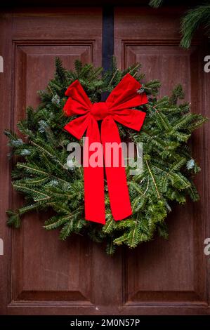 Una foto verticale di una corona di Natale sulla porta con un grande arco rosso su di essa Foto Stock