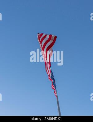 Una grande bandiera americana soffia nel vento contro un cielo blu brillante. Foto Stock