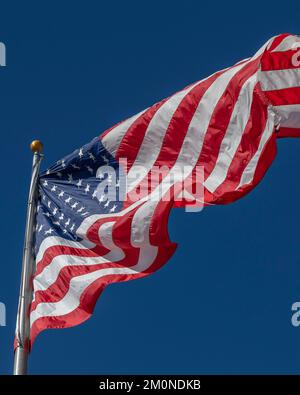 Una grande bandiera americana soffia nel vento contro un cielo blu brillante. Foto Stock