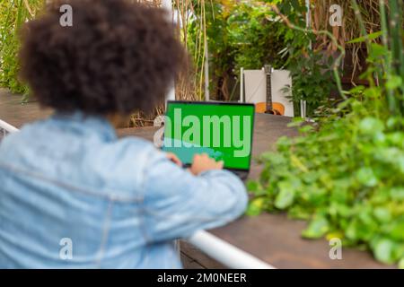 Giovani uomini etnici , vestiti in abiti casual, lavora su un monitor portatile con chiave croma all'aperto, in un'area verde in natura.spazio aperto verde libero Foto Stock