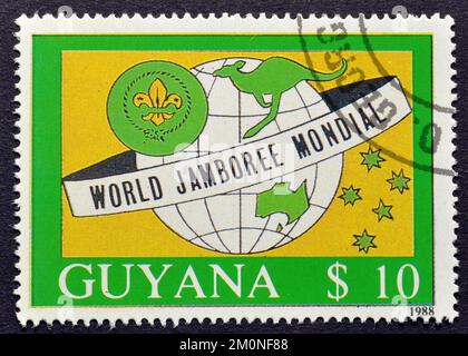 Francobollo cancellato stampato da Guyana, che mostra l'emblema della Terra e dello Scout, promuovendo World Jamboree Mondial, circa 1988. Foto Stock