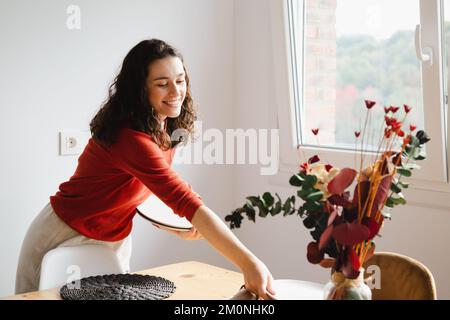 Giovane donna felice che fissa il tavolo per la cena a casa Foto Stock