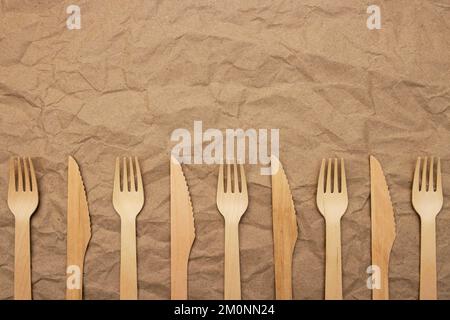 Set di forcelle e coltelli in legno su fondo di carta stropicciato Foto Stock