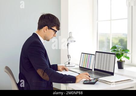 L'uomo d'ufficio lavora con fogli di calcolo sugli schermi dei computer ed effettua calcoli. Foto Stock
