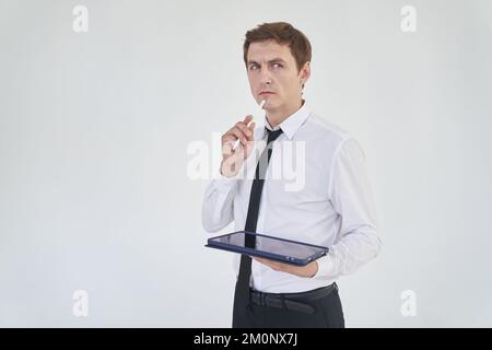 Un giovane lavoratore di ufficio maschile premuroso si trova su uno sfondo leggero con un tablet e una penna. Con spazio per copiare. Foto di alta qualità Foto Stock