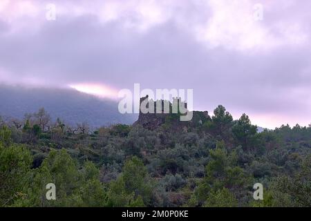 Jinquer, Castellon, Spagna. Rovine di un castello abbandonato in cima alla foresta di mountain.Mediterranean, ulivi, pini, cielo con nuvole tempesta Foto Stock