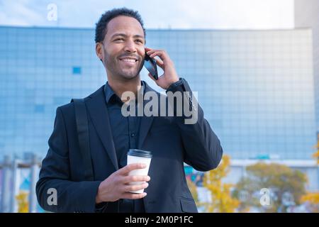 Uomo d'affari afro-americano di successo in tuta sorridente felice parlando con lo smartphone. Foto Stock