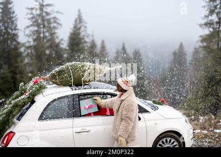 La donna viaggia in auto con regali e albero di Natale sulla strada di montagna Foto Stock