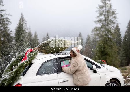 La donna viaggia in auto con regali e albero di Natale sulla strada di montagna Foto Stock