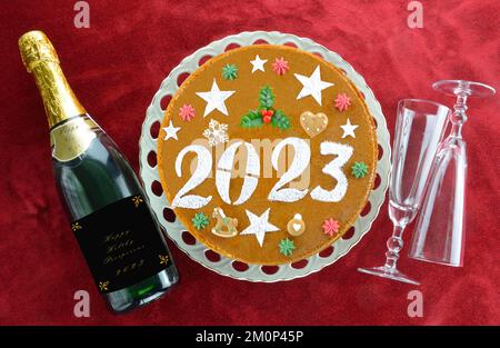 2023 torta di Capodanno , bottiglia di champagne e bicchieri su sfondo di velluto rosso Foto Stock