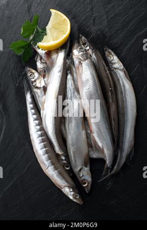 Pescato di fresco piccolo pesce marino su un piatto su uno sfondo grigio cemento con spazio copia. Capelin, pronto per cucinare, con limone, sale marino grosso. In alto vi Foto Stock