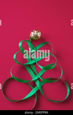 Albero festoso in nastro verde satinato su sfondo rosso. Concetto creativo di Natale per la pubblicità. Colore dell'anno 2023 - Viva Magenta Foto Stock