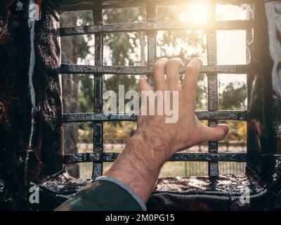 Mano dell'uomo sulla grata di ferro. Concetto di criminale in prigionia o in prigione. Foto Stock