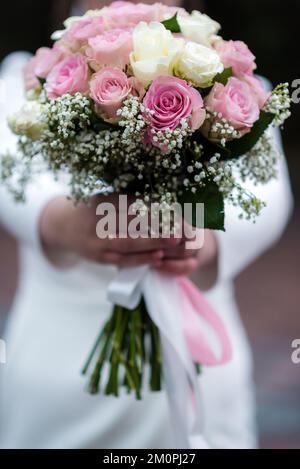 La sposa in un abito da sposa bianco è in possesso di un bouquet di fiori bianchi - peonie, rose. Matrimonio. Sposa e sposo. Delicato bouquet di benvenuto. Bellissima Foto Stock