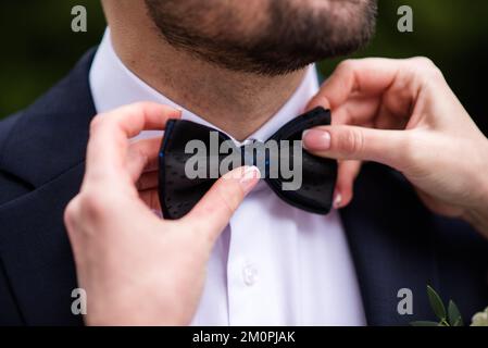 le mani del tirante d'arco dello spazio per lo sposo. eleganti governanti che aiutano a preparare il corpo felice la mattina per la cerimonia di matrimonio. uomo di lusso in camera. w Foto Stock