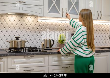 La giovane casalinga carina apre la porta dell'armadio della cucina Foto Stock