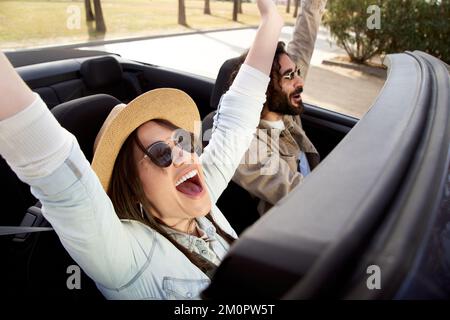 Felici amici di coppia che si divertono a ballare in macchina seduti sul sedile anteriore e a divertirsi in viaggio Foto Stock