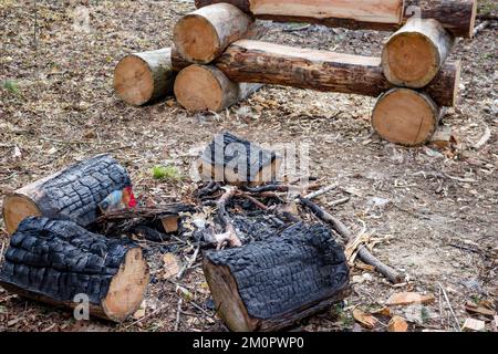 Buca di fuoco fatta di tronchi carbonizzati vicino ad una panca di legno in un campeggio Foto Stock