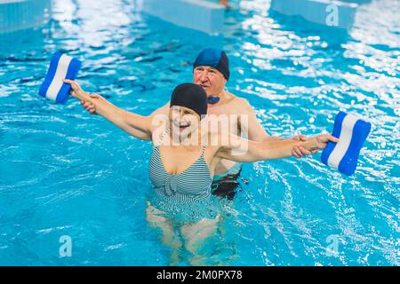 Nonni che si prendono cura della loro salute. Coppia adulta adulta caucasica sposata che fa esercizi di fitness in acqua con boe in piscina. Piscina interna. Foto di alta qualità Foto Stock