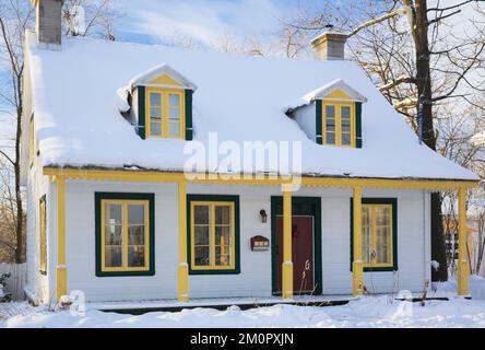 Vecchio bianco anni '1800 con finiture gialle e verdi, casa in stile cottage canadese in inverno. Foto Stock