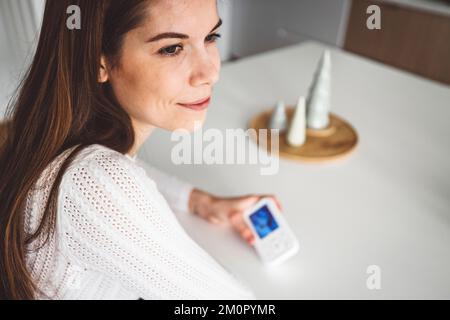 Donna caucasica che tiene in mano una macchina fotografica per bambini, mentre si siede all'isola della cucina Foto Stock