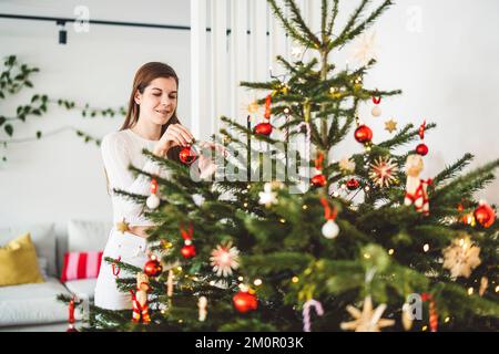 Donna che decora un albero di Natale enorme naturale che mette sugli ornamenti rossi Foto Stock