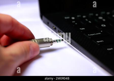 Una persona che collega una spina audio da 3,5mm mm a una presa per cuffie sul lato di un computer portatile. Foto Stock