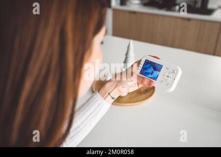 Vista a spalla di una donna irriconoscibile che guarda il baby monitor Foto Stock