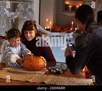 HES che rende la zucca più spaventosa mai vista. un padre che fotografa suo figlio e sua moglie che intagliano una zucca insieme su halloween a casa. Foto Stock