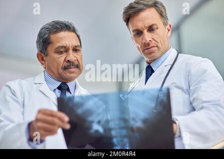 Consultare un collega per un secondo parere. due medici che osservano una radiografia insieme. Foto Stock