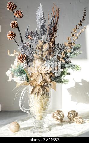 Una composizione floreale invernale di fogliame scintillante in un vaso d'annata di vetro. Foto Stock