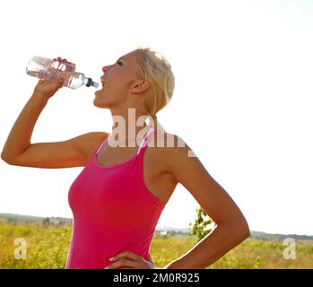 Così assetato dopo quella corsa. Una bella giovane donna in abbigliamento sportivo bere acqua da una bottiglia. Foto Stock