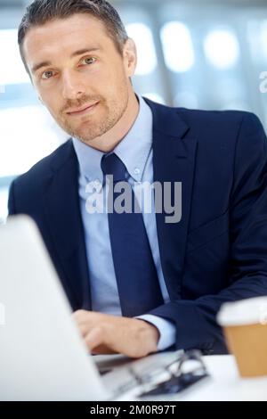 HES un esperto negli affari aziendali. Bell'uomo d'affari maturo che usa il suo computer portatile seduto alla sua scrivania. Foto Stock