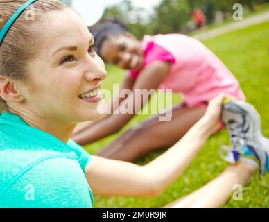 Stretching felice. Primo piano ripresa di un runner femmina che si raffredda sull'erba. Foto Stock