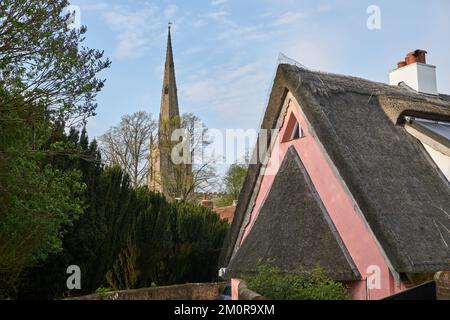 Vecchia casa con tetto in paglia accanto alla guglia della chiesa a Thaxted, Essex, Regno Unito Foto Stock