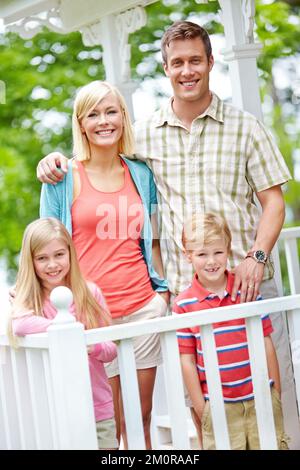 Il perfetto ritratto di famiglia. Una famiglia di quattro in piedi insieme sul loro portico. Foto Stock