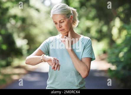 Come sono i miei livelli. una donna matura che usa un orologio e controlla il suo polso mentre si esercita all'aperto. Foto Stock