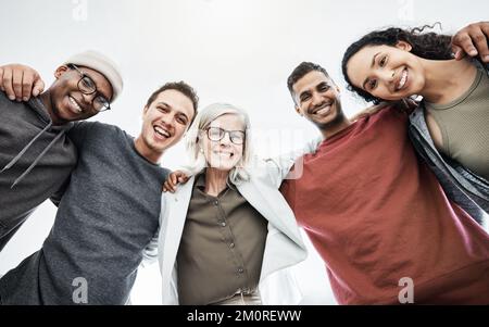 Ritratto ad angolo basso del team di persone in viaggio d'affari che si abbraccia l'un l'altro. Gruppo vario di uomini e donne in piedi in un insieme nel loro ufficio, huddling e. Foto Stock